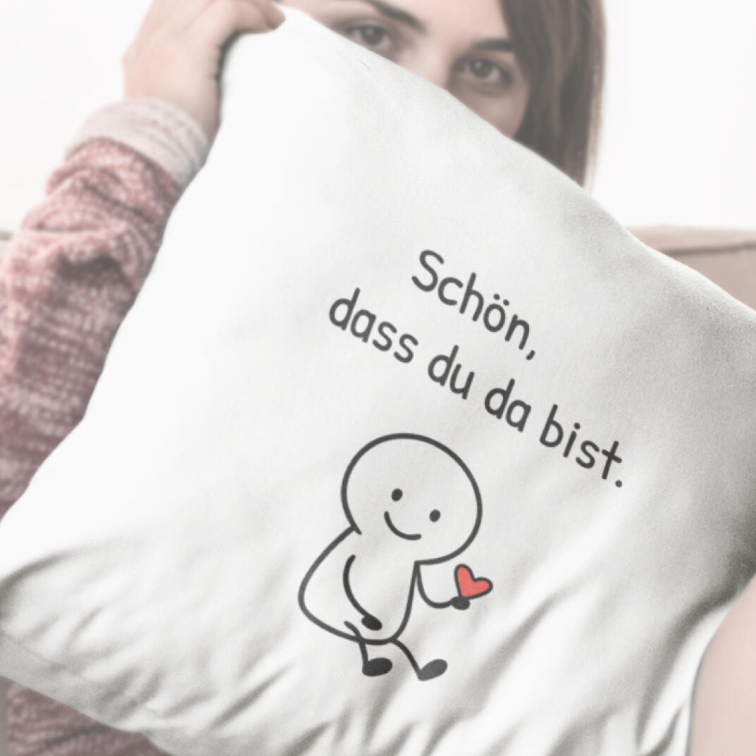 Junge Frau hält helles Kissen mit Strichfigur, Herz und Aufdruck „Schön, dass du da bist.“ – liebevoller Geschenktipp mit Gefühl.