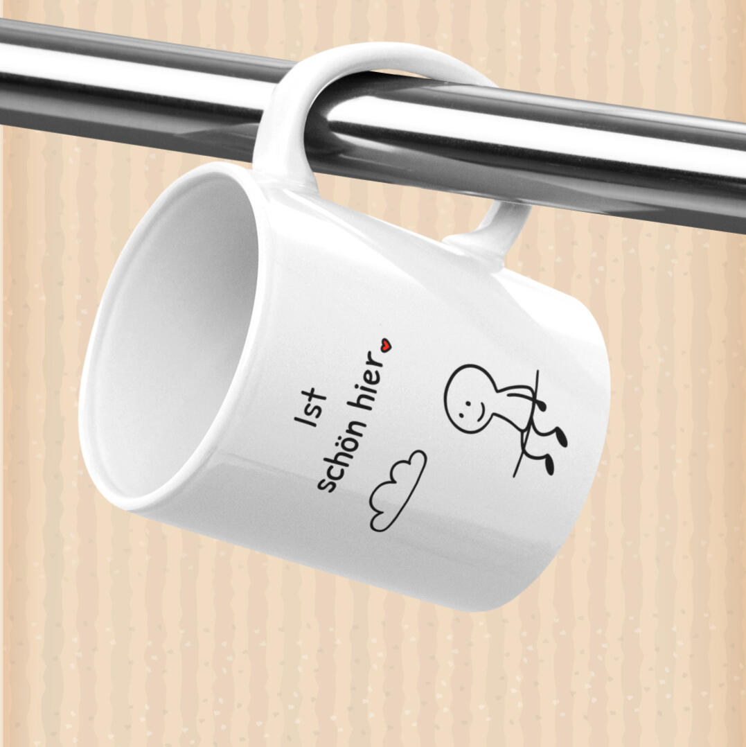 Weiße Tasse hängt am Haken mit Aufdruck „Ist schön hier.“ und kleinem Strichmännchen