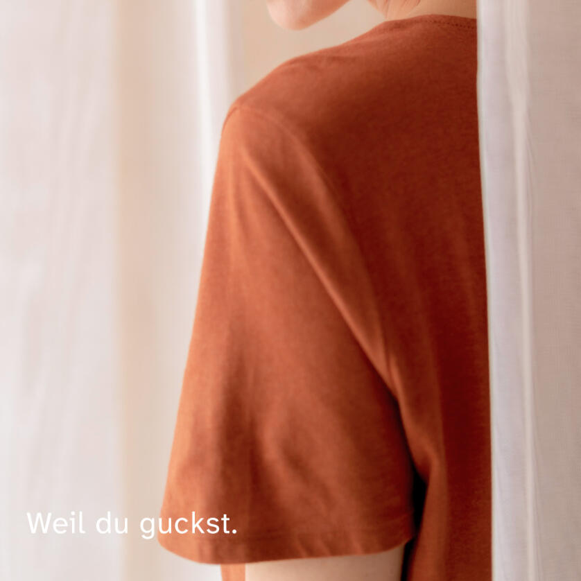 Person steht ruhig am Fenster und blickt nach draußen, darüber der Text „Weil du guckst.“ in schlichter Typografie, reduzierte Szene.