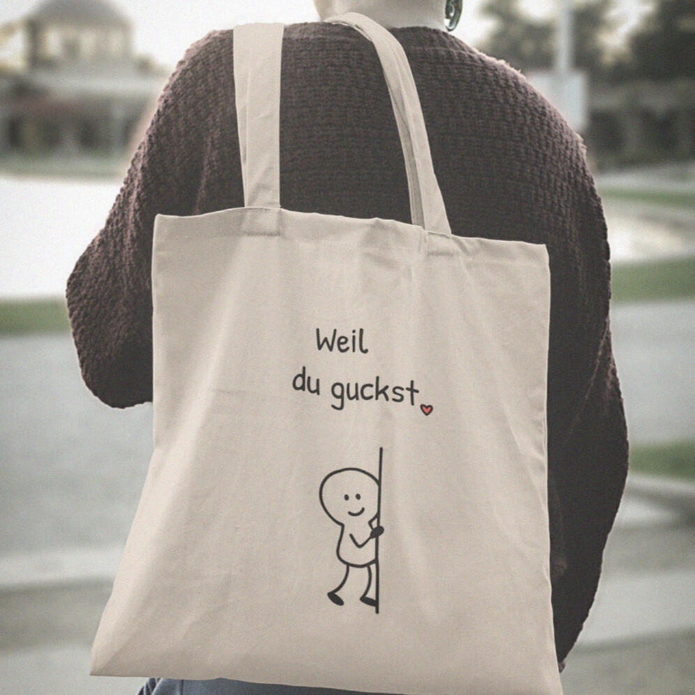 Person nutzt Stoffbeutel mit Figur und dem Spruch „Weil, du guckst“ in ruhiger Alltagsszene.